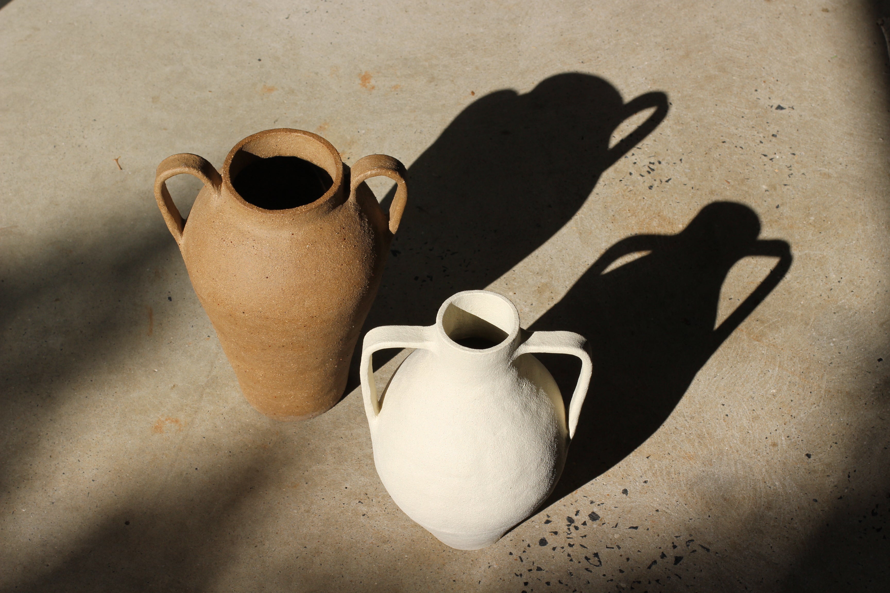 Two ceramic vases, one brown and one white, on a concrete surface.