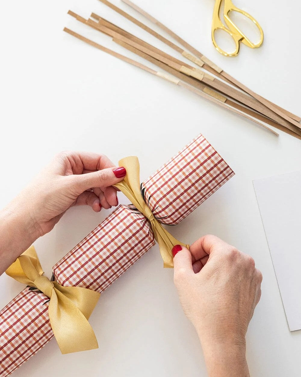 Tying a gold ribbon bow on an Enchanted red check Christmas cracker