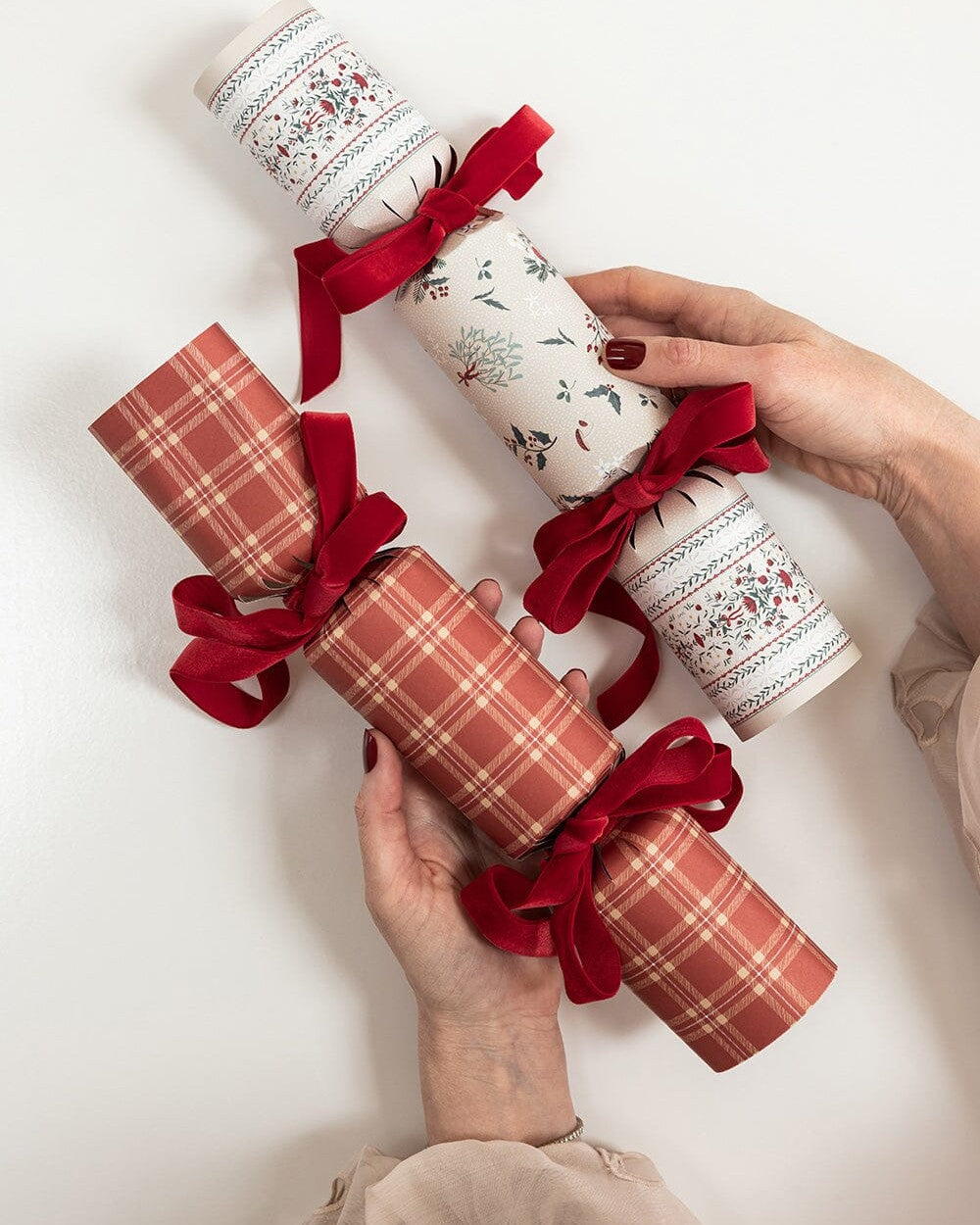 Hands holding Heirloom Holly Christmas crackers tied with red ribbon