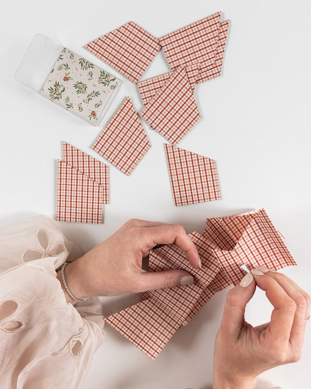 Hands folding Enchanted red check paper crowns beside the box