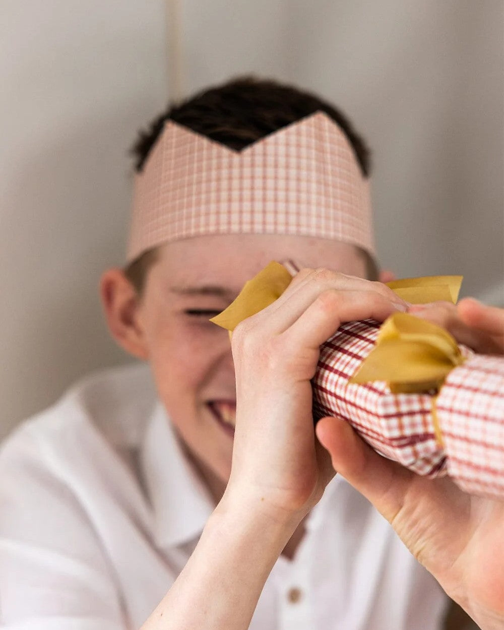 Boy in an Enchanted paper crown laughing as he pulls a Christmas cracker