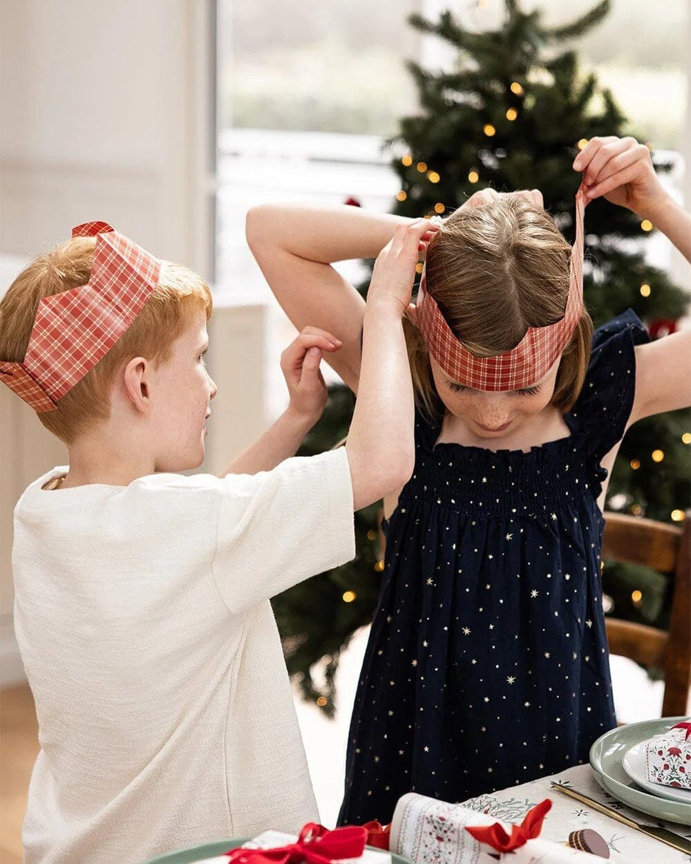 Children wearing Heirloom Holly paper crowns beside a Christmas tree