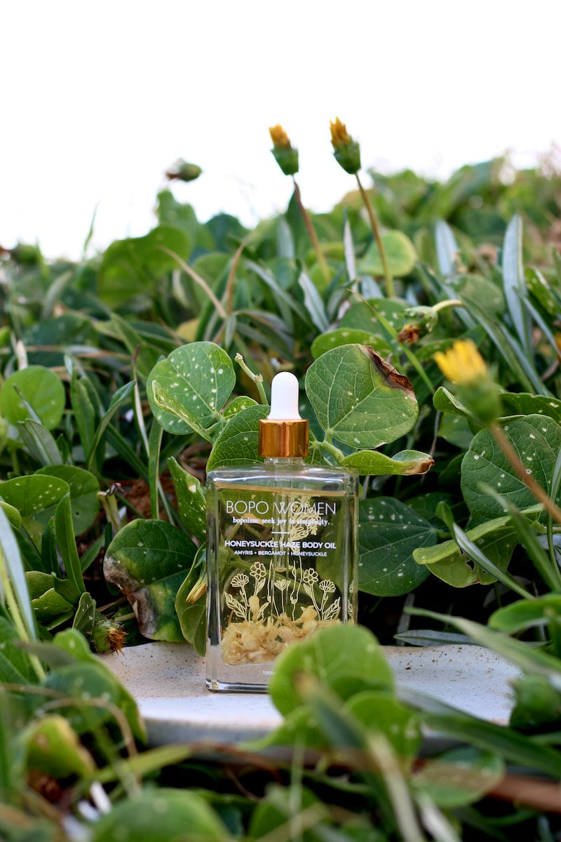 Bopo Women Honeysuckel Haze Bottle of body oil with a dropper on green leaves