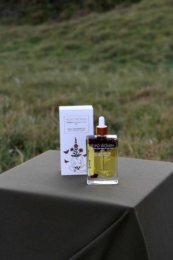 Bottle of Bopo Women Self Love Body Oil with dropper and packaging on a table outdoors.
