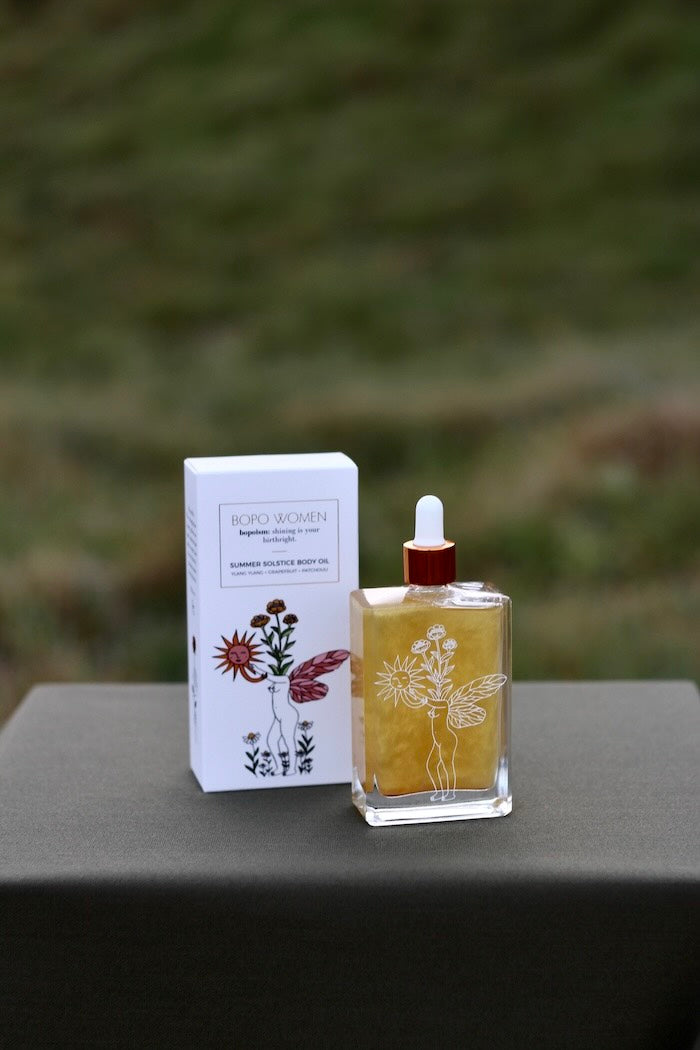 Bottle and box of Bopo Women Summer Solstice on a gray surface with a blurred green background