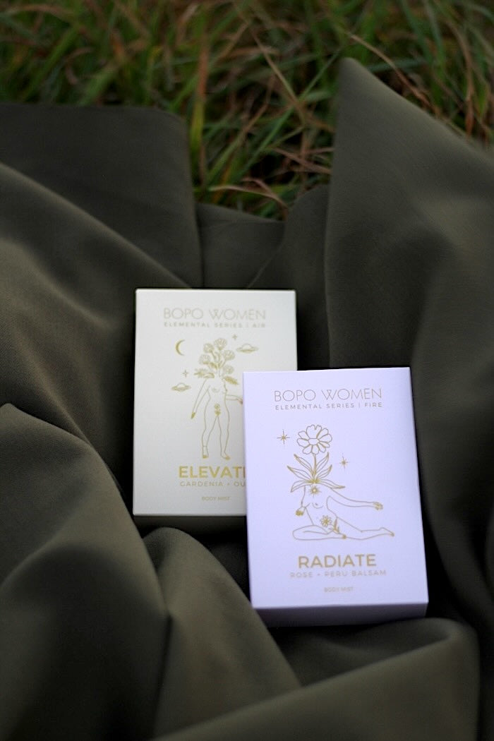 Two Bopo Women Body Sprays with gold text and branding on a dark green natural fabric
