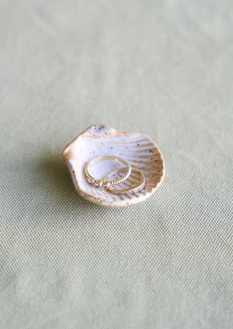 Shell jewelry dish with gold rings on a light green fabric background