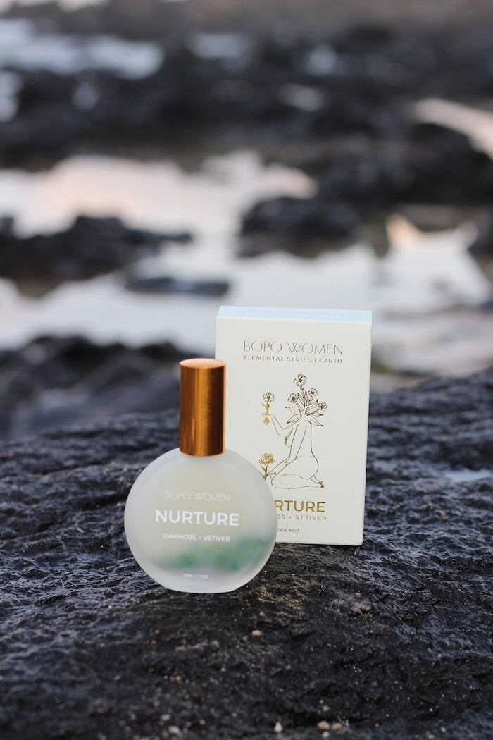Bopo Women Perfume bottle and packaging labeled 'Nurture' on a rocky surface with water in the background at the beach at Black Head in Ballina 