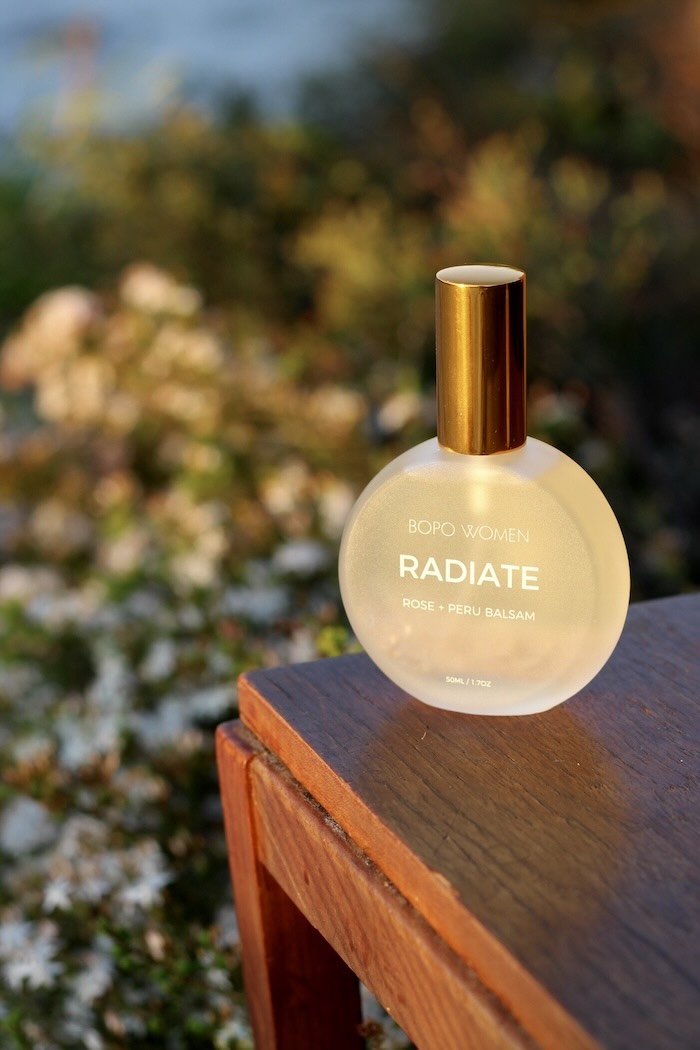 Bottle of 'Radiate' perfume by Bora Women on a wooden surface with a blurred natural background